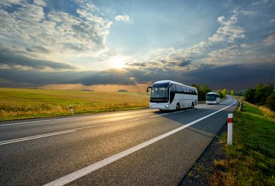 Two white buses traveling on the asphalt road in rural landscape at sunset with dramatic clouds